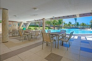 Ein Poolbereich im Freien mit mehreren Tischen und Stühlen, umgeben von Palmen und freiem Blick auf den Pool.