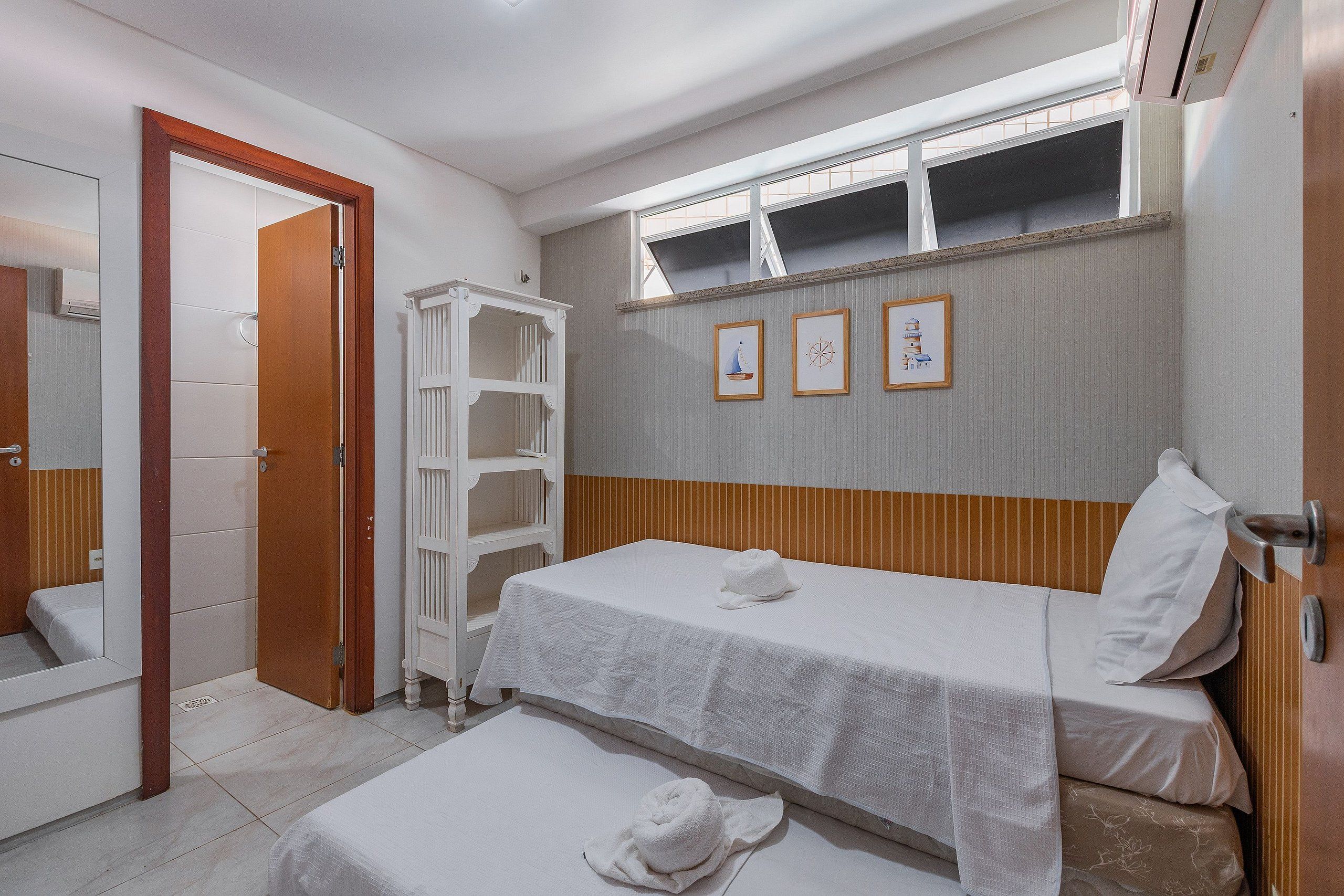 Quarto de hotel com uma cama de solteiro, uma pequena mesa de cabeceira, um espelho e um guarda-roupa.