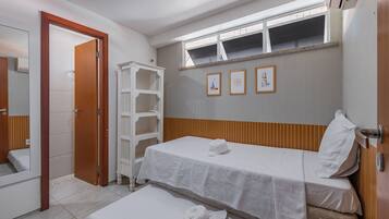 Quarto de hotel com uma cama de solteiro, uma pequena mesa de cabeceira, um espelho e um guarda-roupa.
