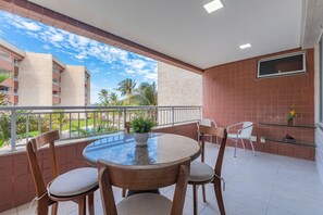A balcony with a round table and chairs, a potted plant, and a TV mounted on the wall. - Scopa Beach #c5-200 - On the Sand by Carpediem (Aquiraz)
