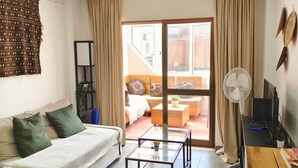 En moderne stue med sofa, sofabord, fjernsyn og en skydedør til en balkon.