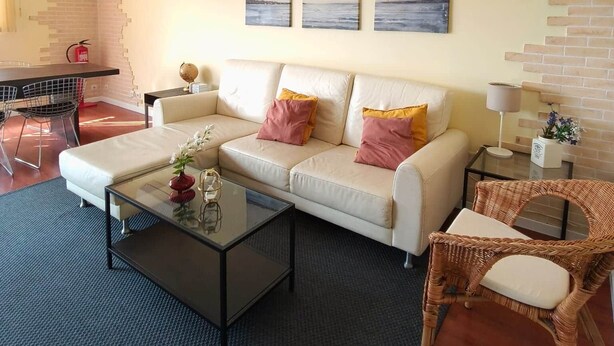 A living room with a sofa, coffee table, wicker chair, and artwork on the wall. - Mivô | Cascais Sunshine (Cascais)