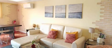 A living room with a sofa, coffee table, wicker chair, and artwork on the wall.