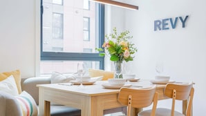 Un comedor con una mesa de madera preparada para dos personas, un florero con flores y un letrero que dice 'REVY' en la pared.