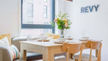 A dining area with a wooden table set for two, a vase with flowers, and a 'REVY' sign on the wall.