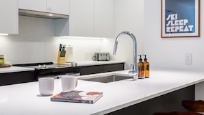 Una cocina moderna con encimera blanca, un lavamanos de acero inoxidable, un tostador y un cuadro en la pared.