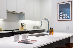 A modern kitchen with a white countertop, a stainless steel sink, a toaster, and a framed picture on the wall. - Beutts Hygge House - Charming One-Bedroom Condo (Revelstoke)