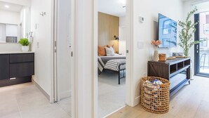 Un interior moderno con cocina, un dormitorio con cama y mesita de noche, televisión y un ventanal grande.