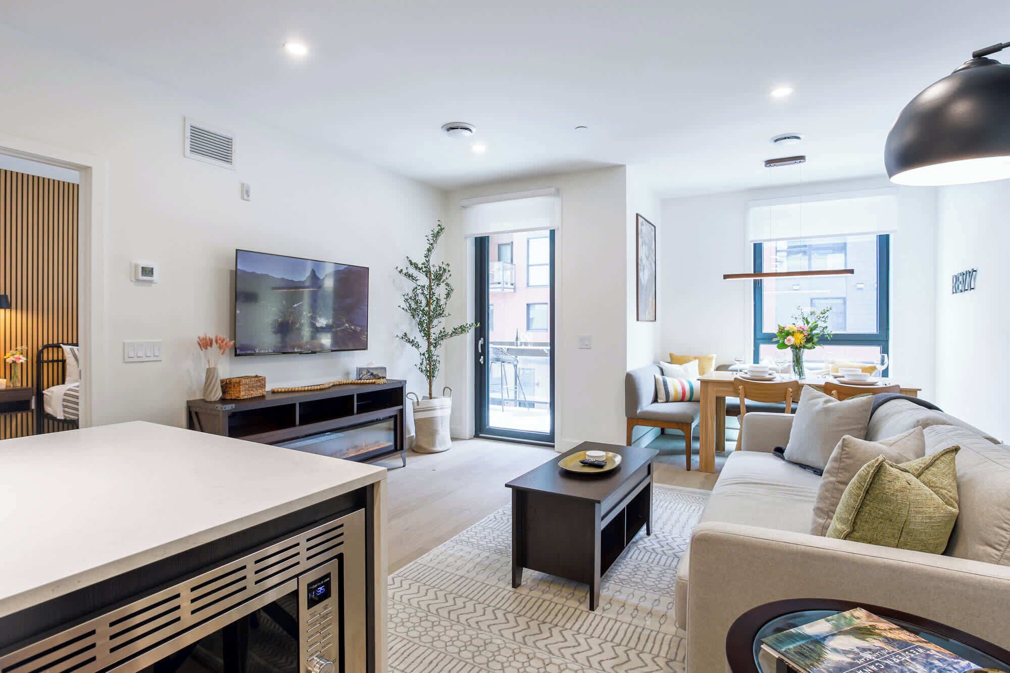 A modern living room with a TV, sofa, dining area, and a large window.