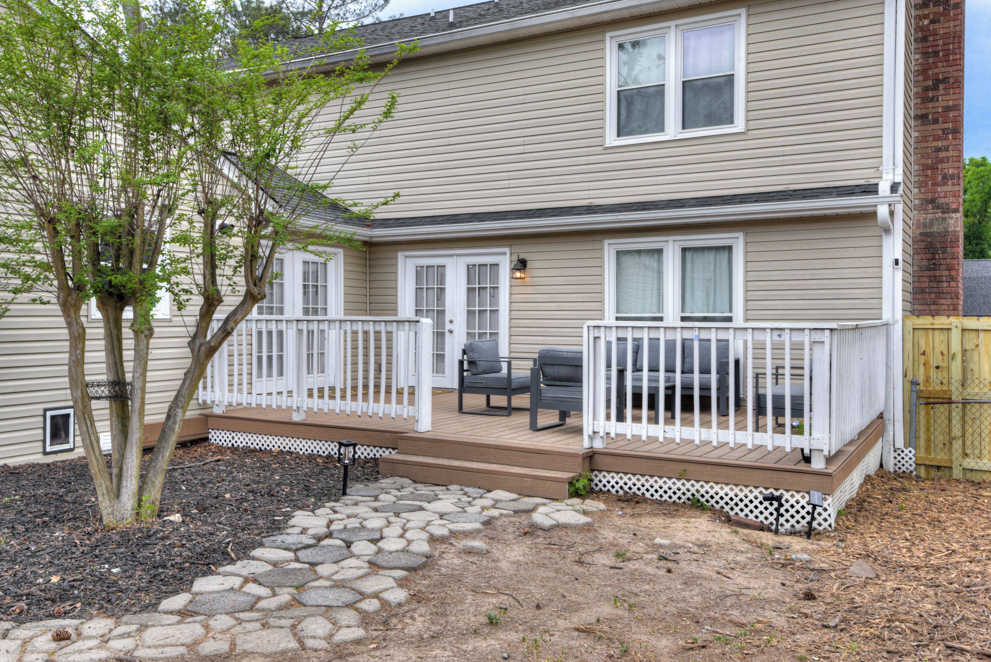 A two-story house with a deck, outdoor seating, and a small tree.