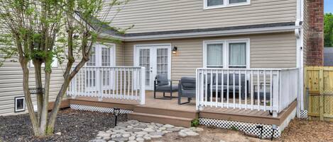 A two-story house with a deck, outdoor seating, and a small tree.