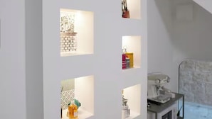 Quarto com parede branca e várias prateleiras iluminadas exibindo diversos objetos.