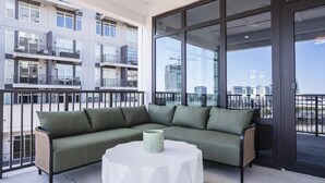 Un balcon avec un canapé vert et une table blanche, donnant sur un paysage urbain.