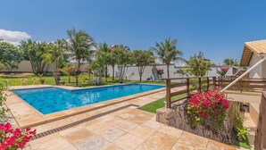 A rectangular swimming pool with a tiled deck, surrounded by palm trees and a grassy area. - Casa Vento - Your Exclusive Refuge by Carpediem (Caucaia)
