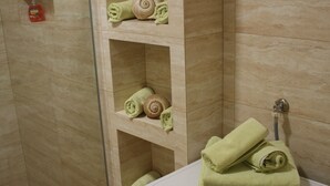 A bathroom with a washing machine, shelves with folded towels, and a soap dispenser. - Three Bedroom Apartment with Sea View and Terrace (Dubrovnik)