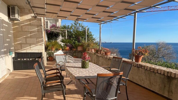 An outdoor patio with a table and chairs, potted plants, and a view of the sea. - Three Bedroom Apartment with Sea View and Terrace (Dubrovnik)