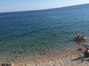 A beach with clear water, a rocky shore, and a small inflatable boat with two people. - Apartments Bozena - Two bedroom apartment (Krk)