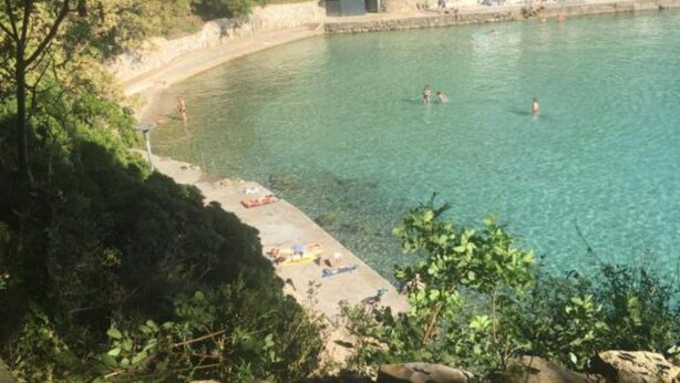 Ein Küstenstrand mit klarem Wasser, einem Sandufer und einem kleinen Gebäude, wahrscheinlich eine Einrichtung oder ein Restaurant.