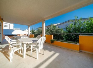 Un patio techado al aire libre con una mesa y sillas, vistas de los edificios circundantes y un cielo despejado.