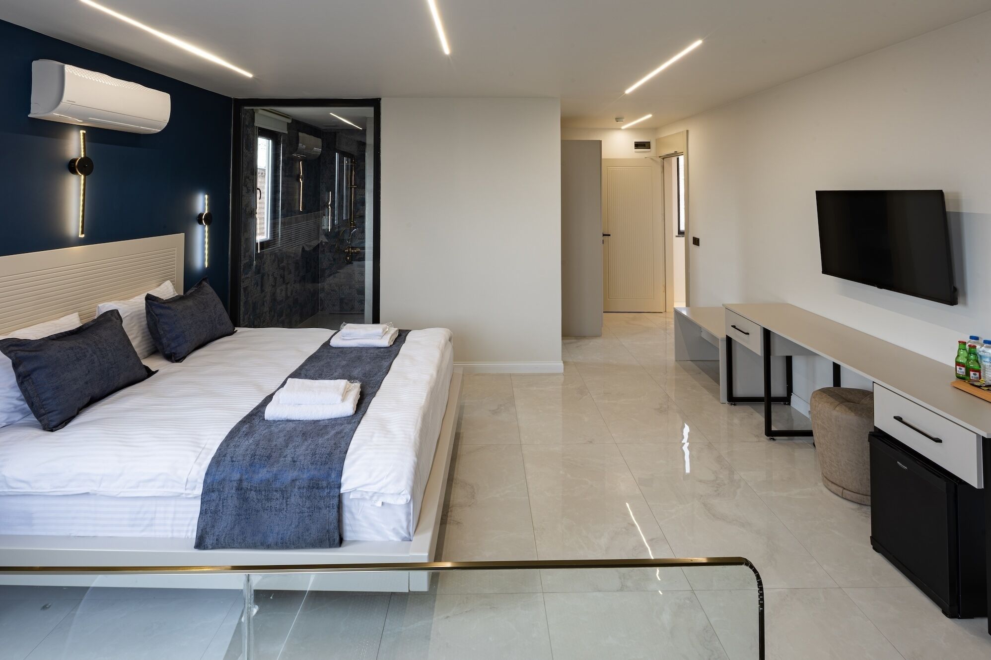 Una habitación de hotel moderna con cama, mesita de noche, televisor y baño con ducha y espejo.
