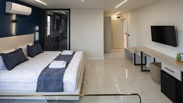 Una habitación de hotel moderna con cama, mesita de noche, televisor y baño con ducha y espejo.