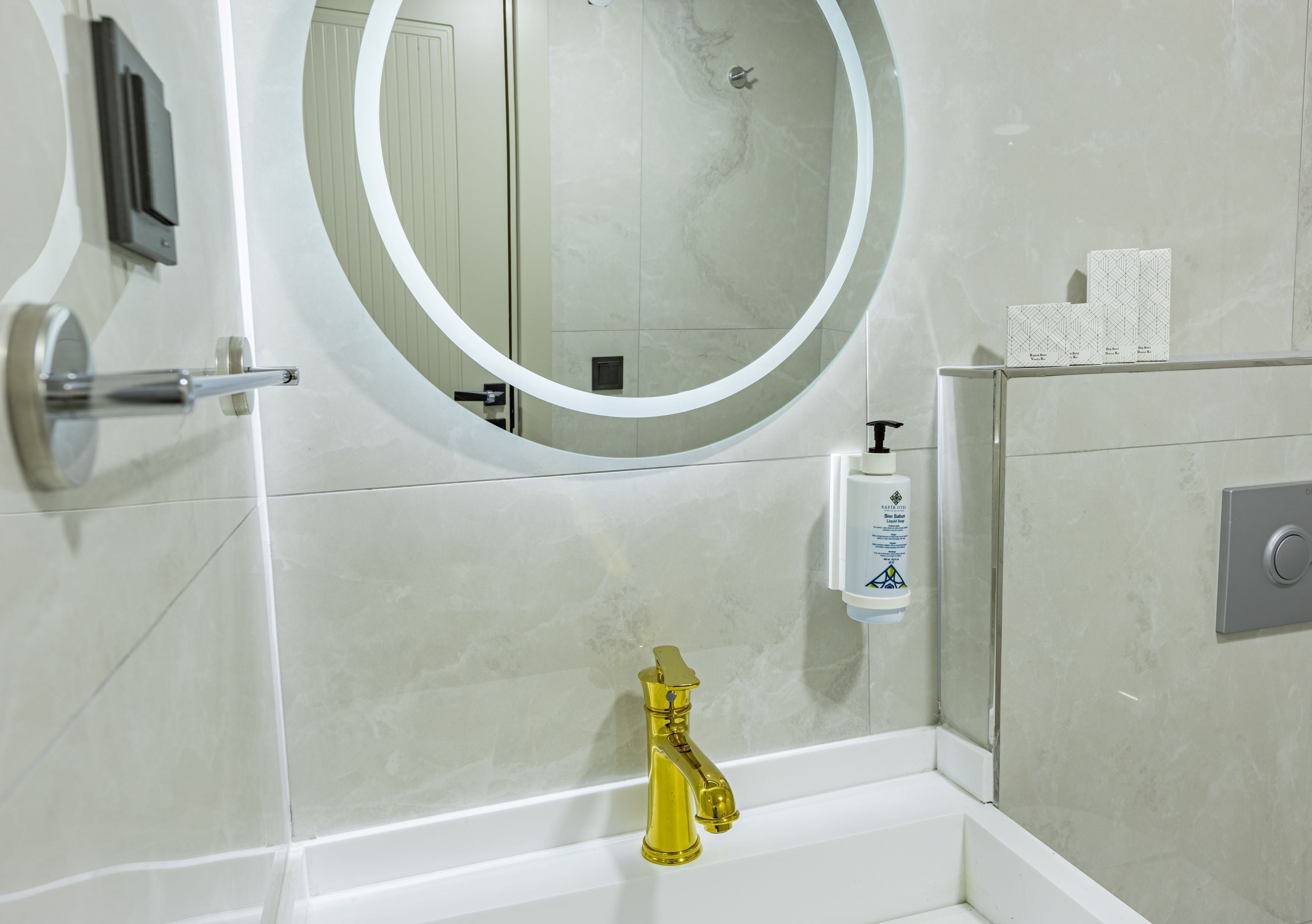 A bathroom with a round mirror, a gold faucet, and a soap dispenser on the wall.