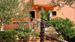 Un bâtiment à l’extérieur recouvert d’enduit, doté d’un balcon avec une balustrade et agrémenté de diverses plantes, dont un palmier.