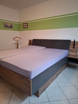 Un lit simple avec un cadre en bois et un matelas gris, dans une pièce aux murs verts et blancs.