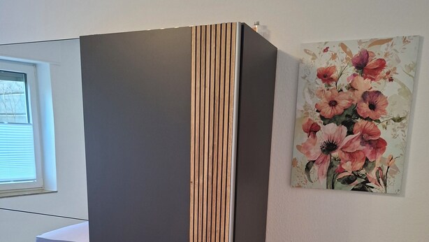 A modern bedroom with a bed, a wardrobe, a small wooden chest, and a floral painting on the wall. - Vacation apartment Zülpich-Nähe Seepark (Zülpich)