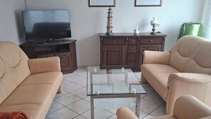 A living room with two beige sofas, a glass coffee table, a TV on a wooden cabinet, and two framed pictures on the wall. - Vacation apartment Zülpich-Nähe Seepark (Zülpich)