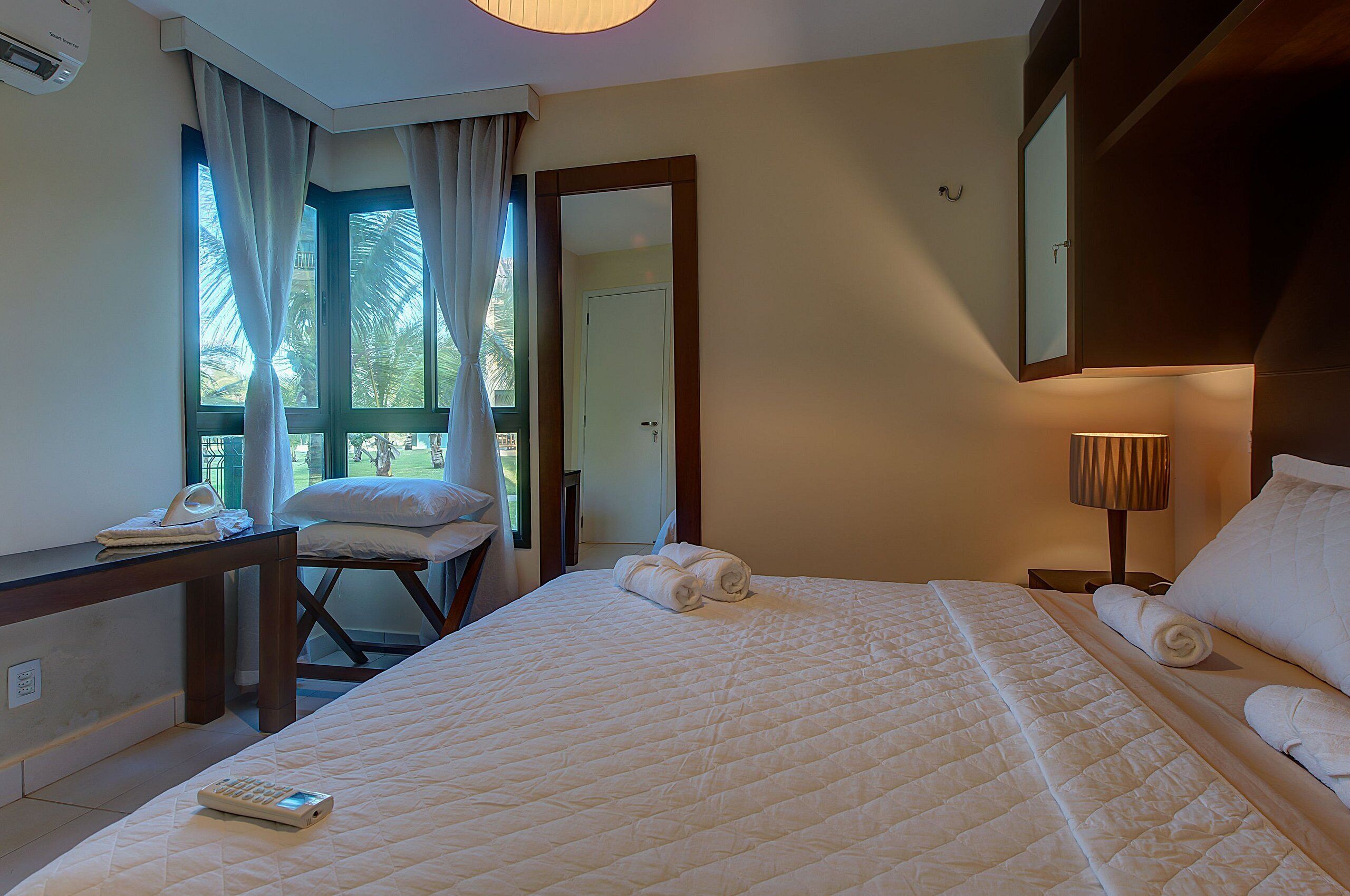 A hotel room with a bed, a desk, a chair, a lamp, and a window with curtains.