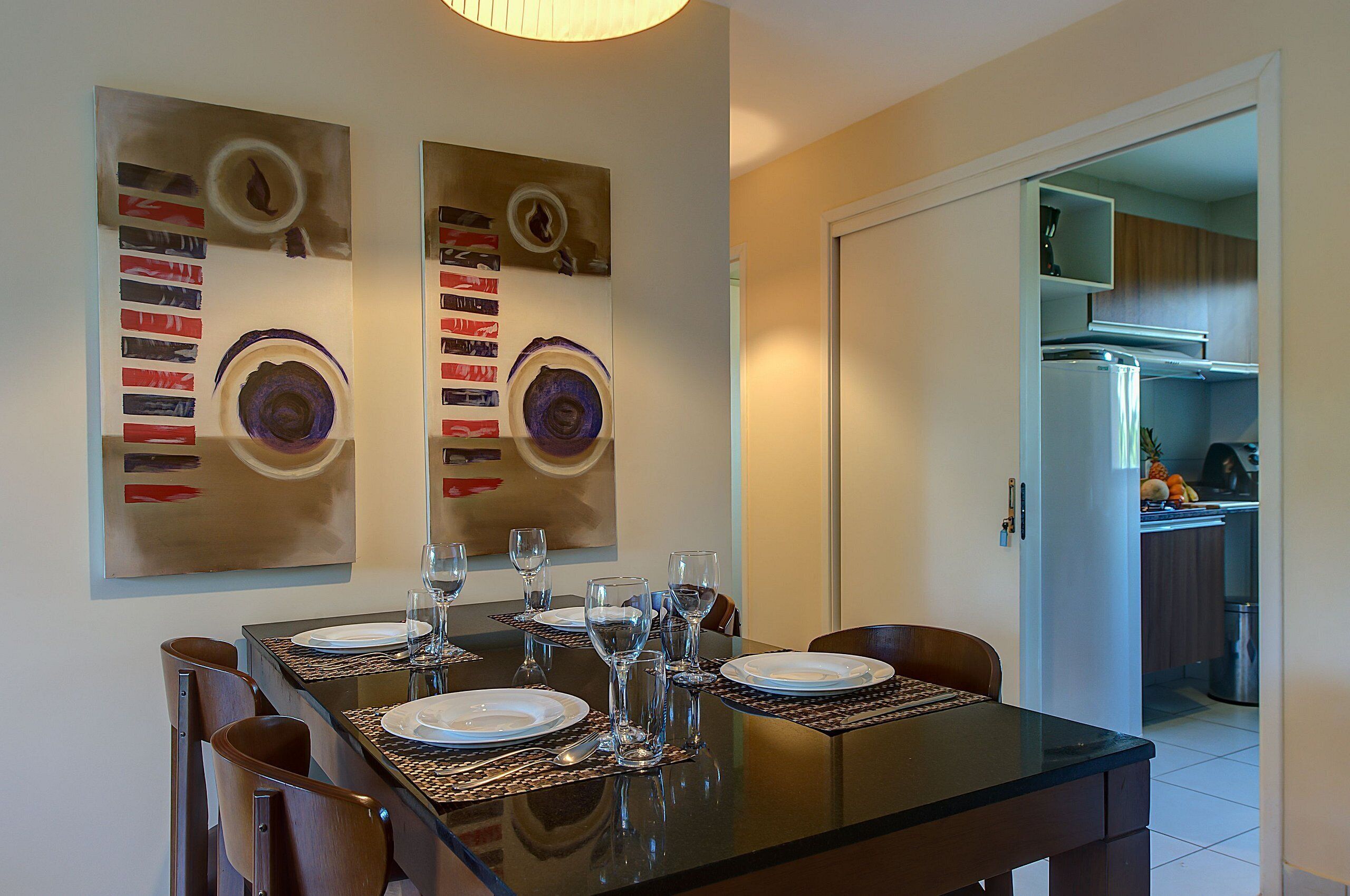 Een eetruimte met een glazen tafel, stoelen en een keuken die zichtbaar is door een open deur.
