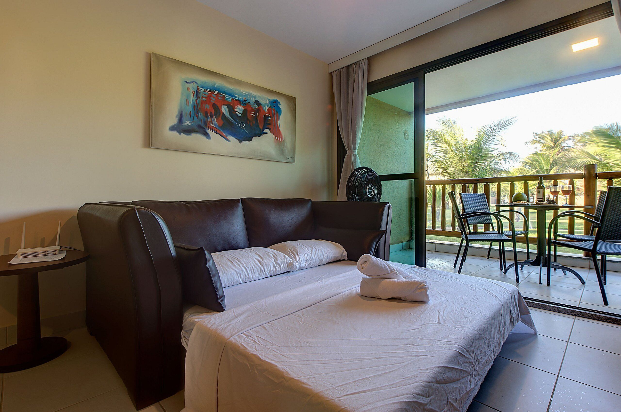 Una habitación de hotel con una cama grande, una mesita con un ordenador portátil y un balcón con sillas y una mesa.