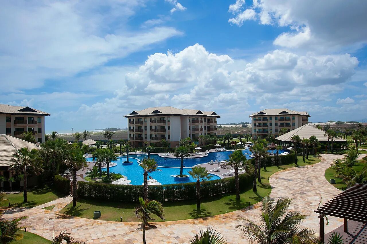 Un resort con piscina central, varias construcciones y palmeras.
