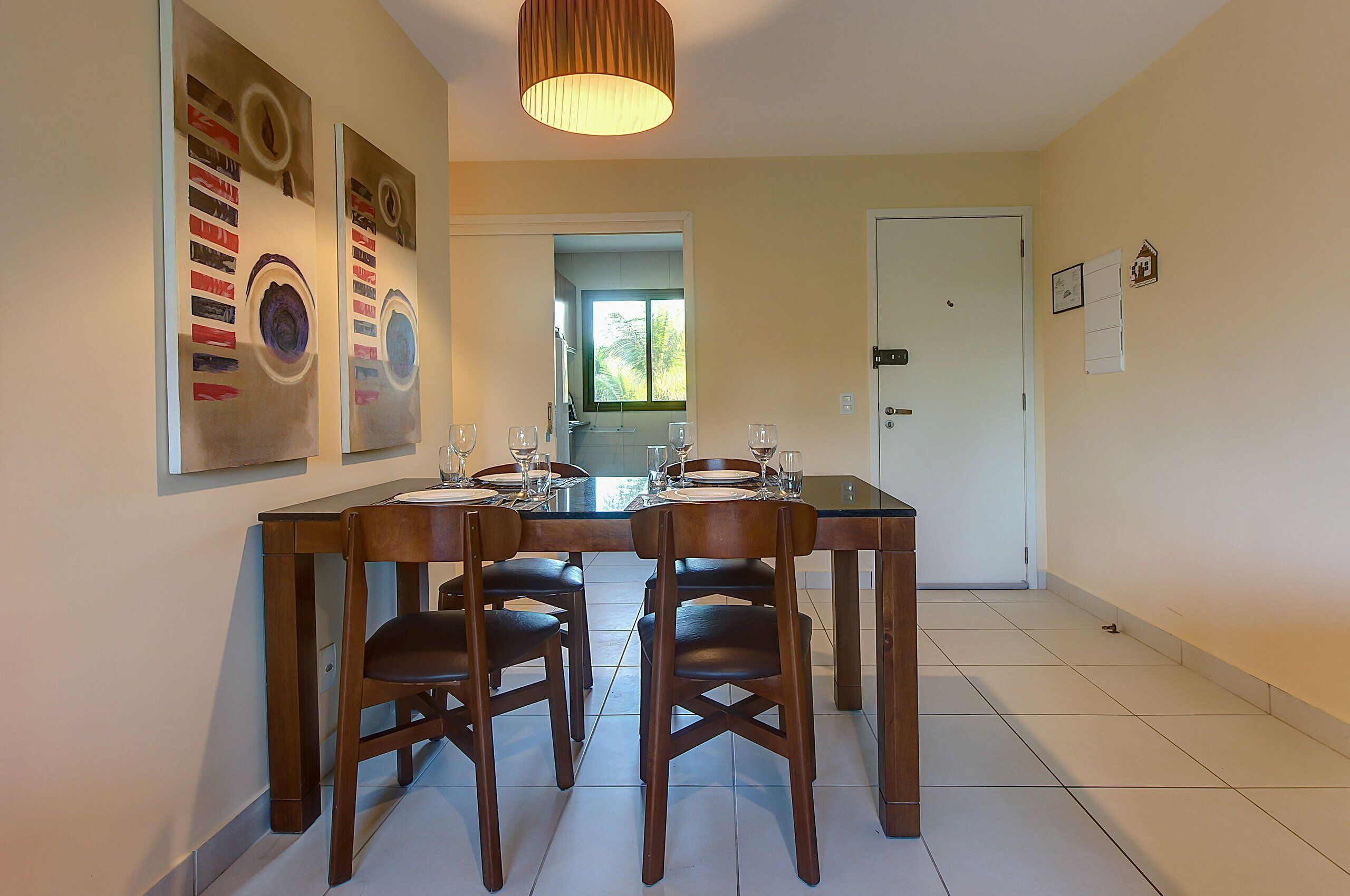 A dining area with a wooden table and chairs, a hanging light fixture, and artwork on the walls.