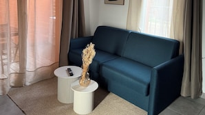 Een moderne woonkamer met een blauwe bank, twee bijzettafels, een decoratieve vaas en een plafondlamp.