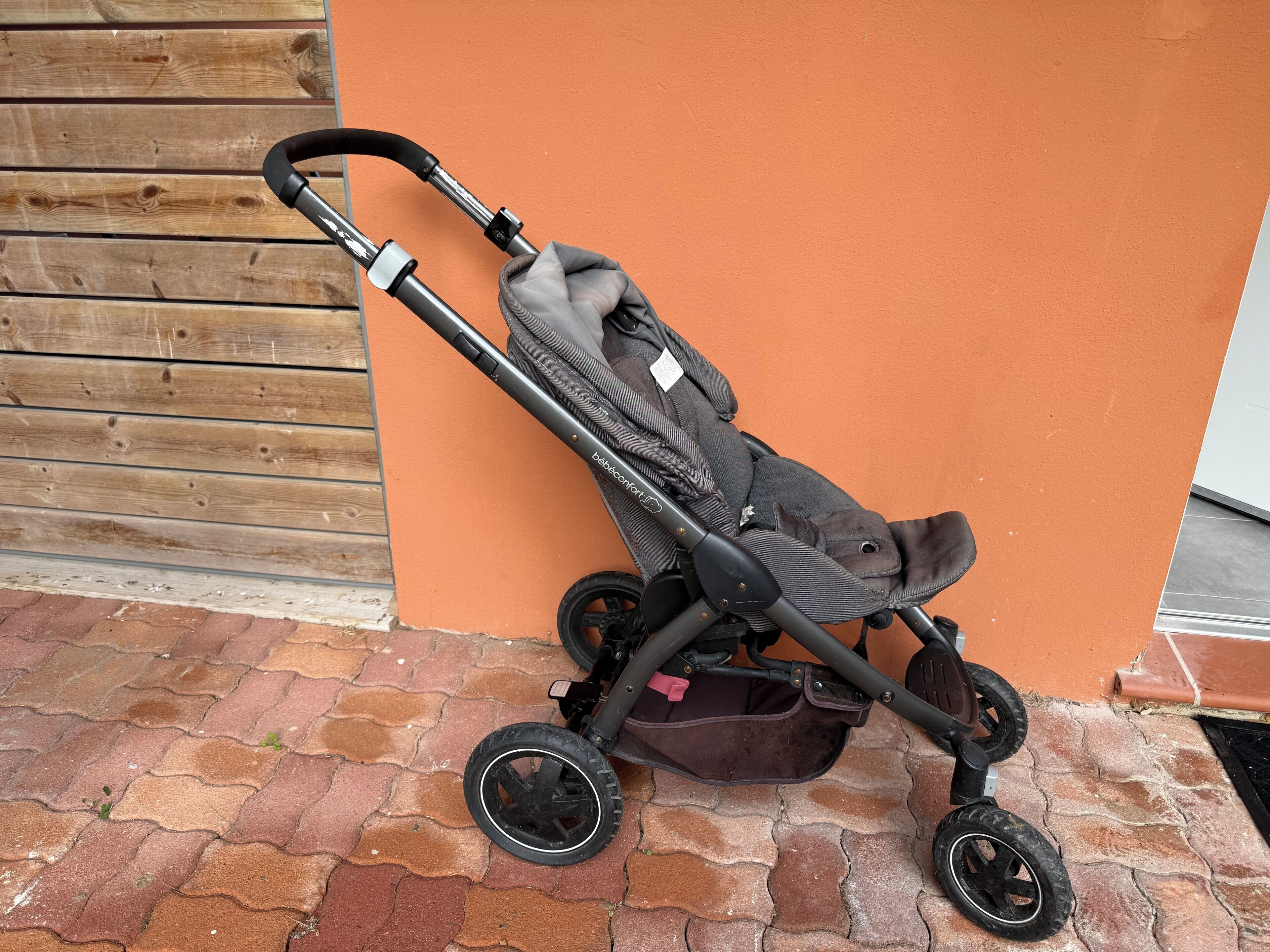 A stroller parked against a wooden wall and orange surface.