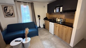 Een moderne woonkamer met een blauwe bank, een klein bijzettafeltje en een decoratieve vaas. Grenzend hieraan een compacte keuken met houten kasten, een magnetron en een broodrooster.