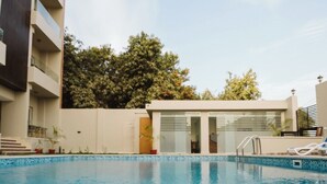 En swimmingpool med en klar blå vandoverflade, omgivet af en moderne bygning med et fladt tag og en overdækket indgang.