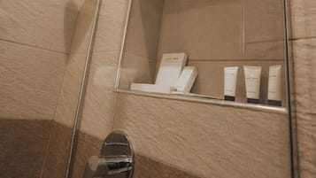 Un baño moderno con cabina de ducha de vidrio, ducha de mano, repisa integrada con artículos de aseo y un espejo.