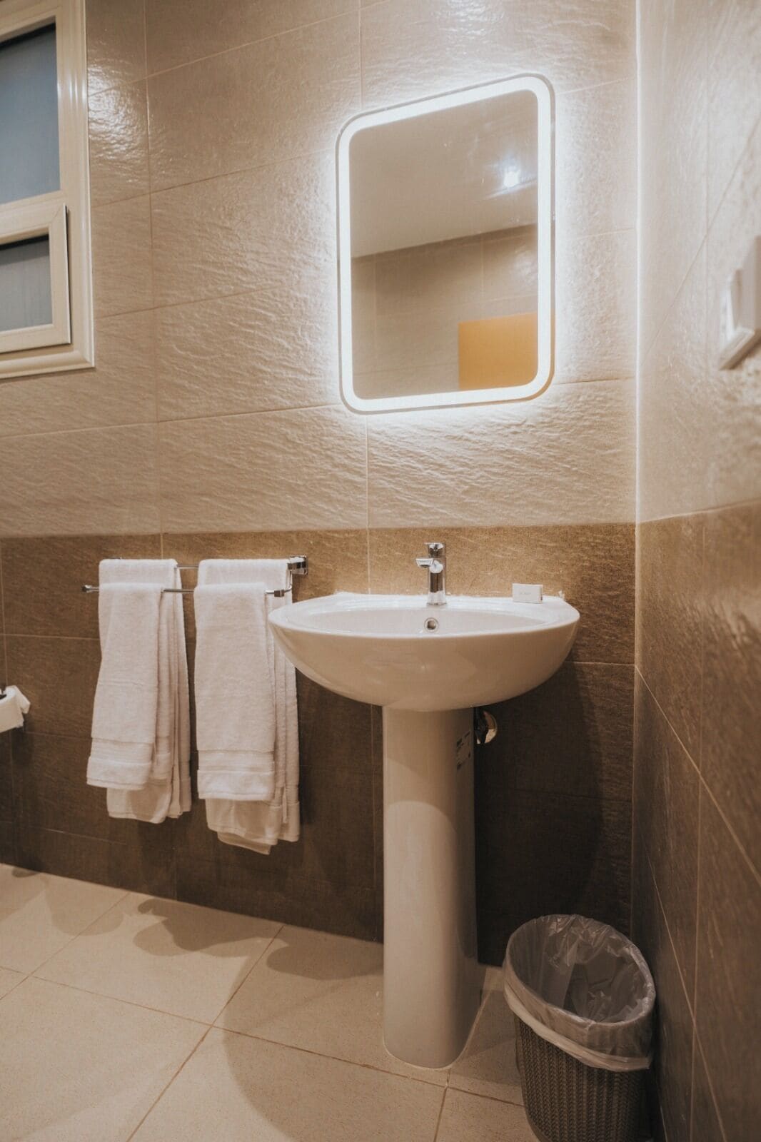 A bathroom with a pedestal sink, a mirror, and two towels hanging on a rack.