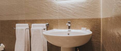A bathroom with a pedestal sink, a mirror, and two towels hanging on a rack.