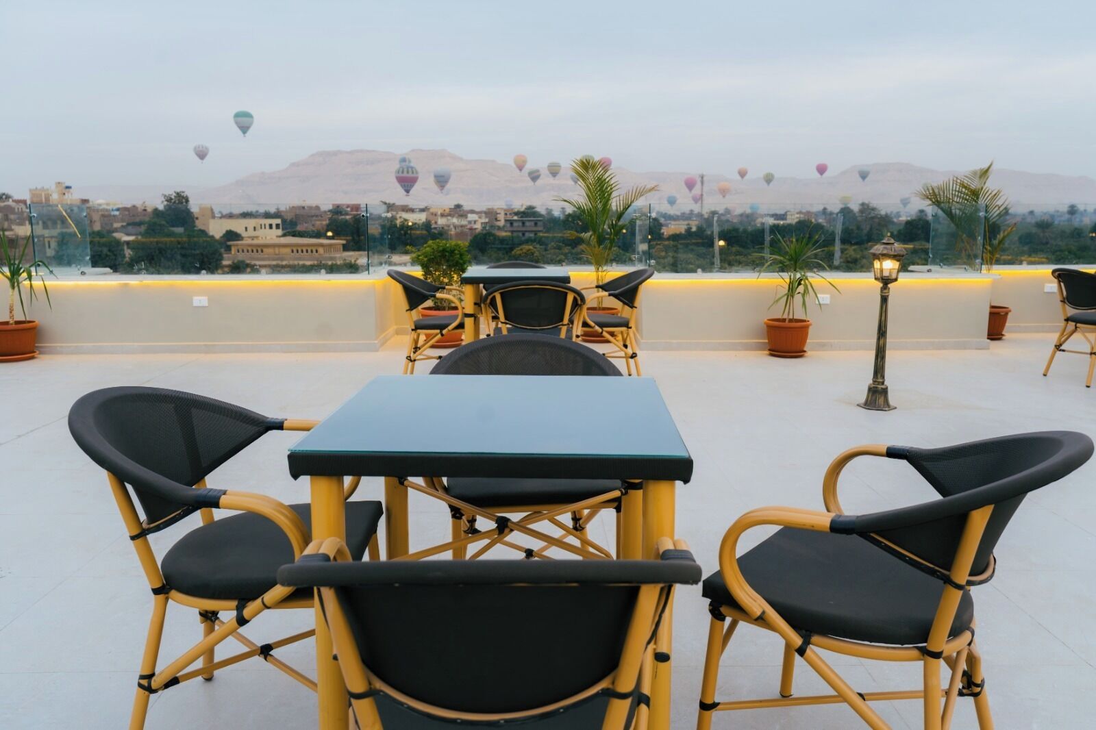 An outdoor seating area with tables and chairs, overlooking a cityscape with mountains in the background.