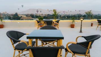 An outdoor seating area with tables and chairs, overlooking a cityscape with mountains in the background.