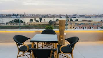 Una terraza con mesa y sillas que da a un río con barcos, edificios y un paisaje urbano al fondo.