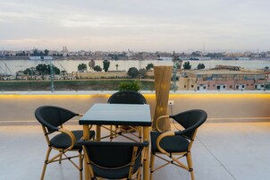 Una terraza con mesa y sillas que da a un río con barcos, edificios y un paisaje urbano al fondo.