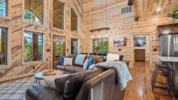 Ein geräumiges Wohnzimmer mit einer Ledersofa, Holzwänden, großen Fenstern und einer Küchenzeile inklusive Kühlschrank.