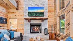 Ein gemütliches Blockhaus-Interieur mit Kamin aus Stein, einem angebrachten Fernseher und einer komfortablen Sitzecke.