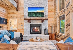 A cozy cabin interior with a stone fireplace, a mounted TV, and a comfortable seating area. - NEW! Hot Tub, Fire Pit, Games, Near Beavers Bend (Broken Bow)