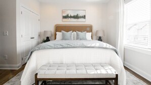 A bedroom with a bed, bedside lamps, a bench, a painting on the wall, and a window with blinds. - Auburn Elite Retreat (Opelika)